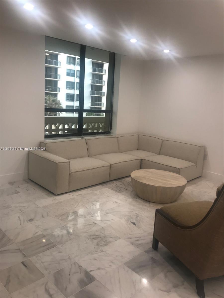 A living room features a beige sectional sofa, a round wooden coffee table, and marble flooring — 10185 Collins Ave # 516, Bal Harbour FL 33154, BAL HARBOUR, FL