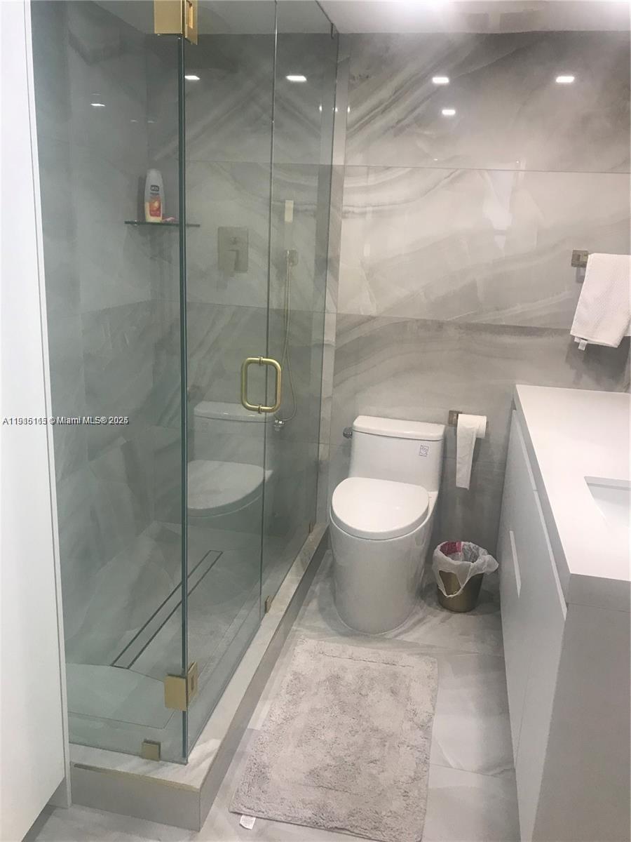 A modern bathroom features a glass-enclosed shower, a white toilet, and gray marble-style tiling — 10185 Collins Ave # 516, Bal Harbour FL 33154, BAL HARBOUR, FL