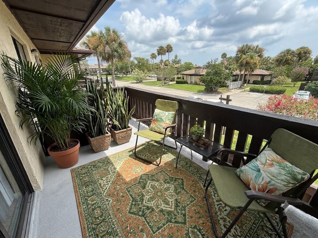 A balcony features a patterned rug, two chairs, a small table, and several potted plants — 42 CLUB HOUSE DRIVE UNIT 207, PALM COAST, FL