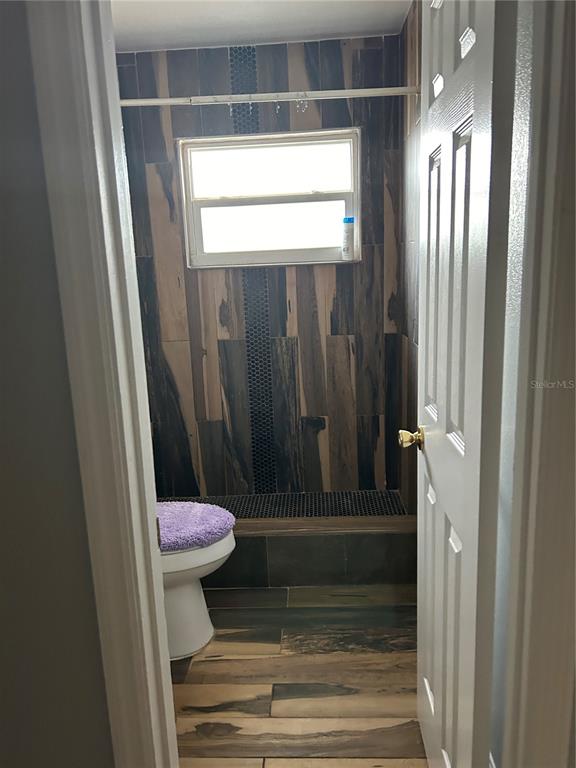 A bathroom features wood-look tile walls and flooring with a central black mosaic accent strip — 7423 SE 226TH TERRACE, HAWTHORNE, FL