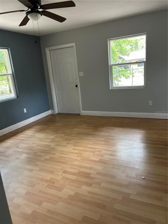 An empty room with light wood-look flooring, gray walls, a ceiling fan, and a door — 7423 SE 226TH TERRACE, HAWTHORNE, FL