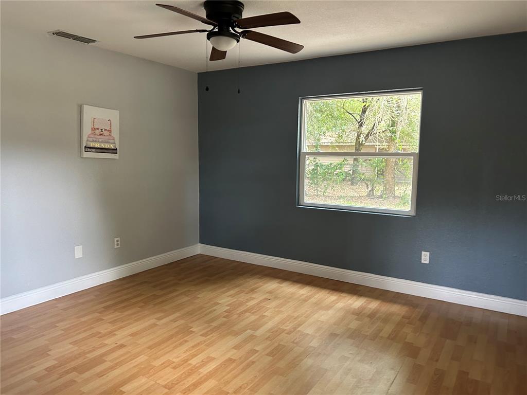 An empty bedroom features light wood flooring, a ceiling fan, and a dark accent wall — 7423 SE 226TH TERRACE, HAWTHORNE, FL