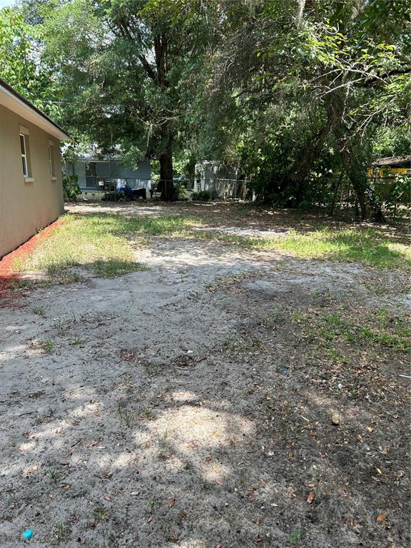 An exterior view of a sandy backyard with trees and a tan house wall — 7423 SE 226TH TERRACE, HAWTHORNE, FL