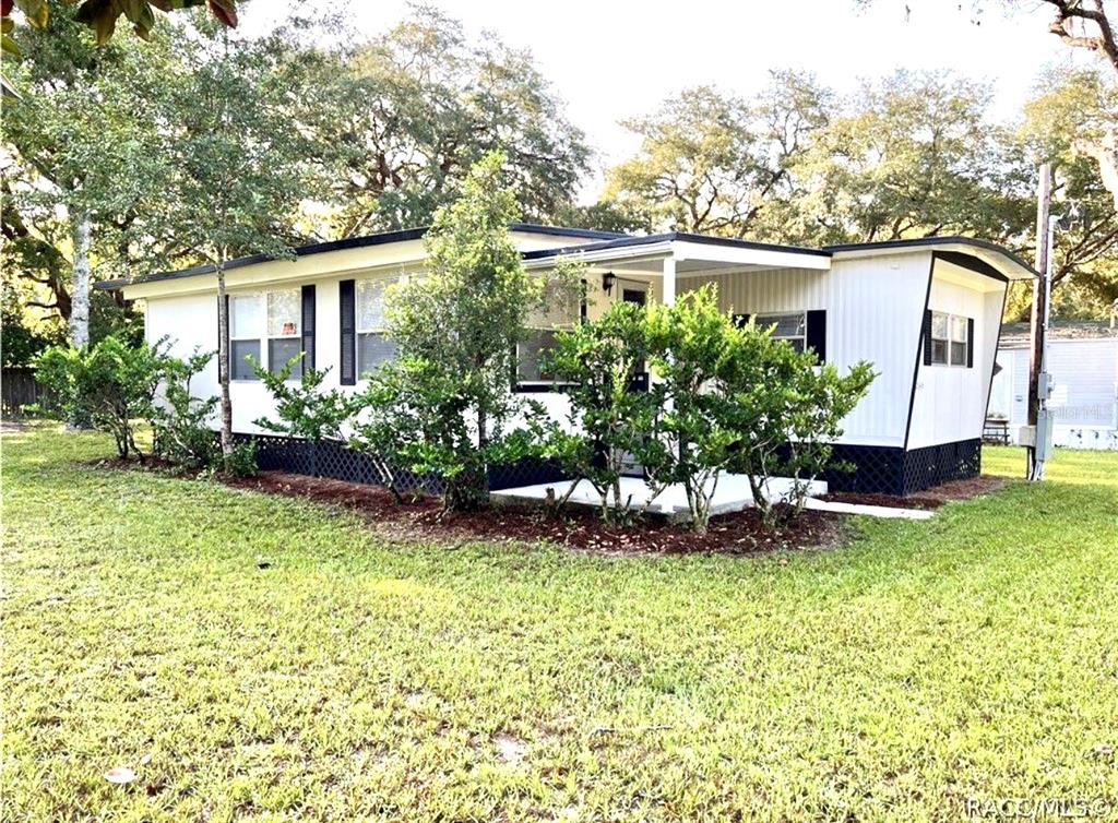 A single-story manufactured home with white siding, a covered porch, and surrounding landscaping — 3249 S CALAIS TERRACE, HOMOSASSA, FL