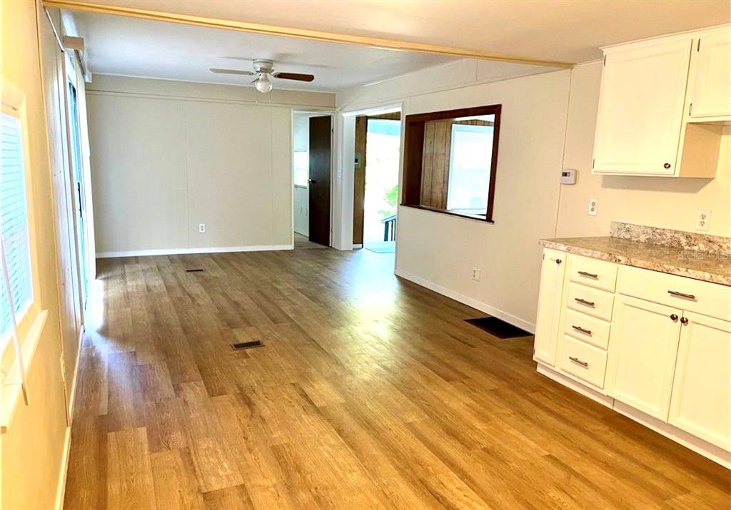 An open-concept living area features wood-look flooring, white kitchen cabinets, and a ceiling fan — 3249 S CALAIS TERRACE, HOMOSASSA, FL