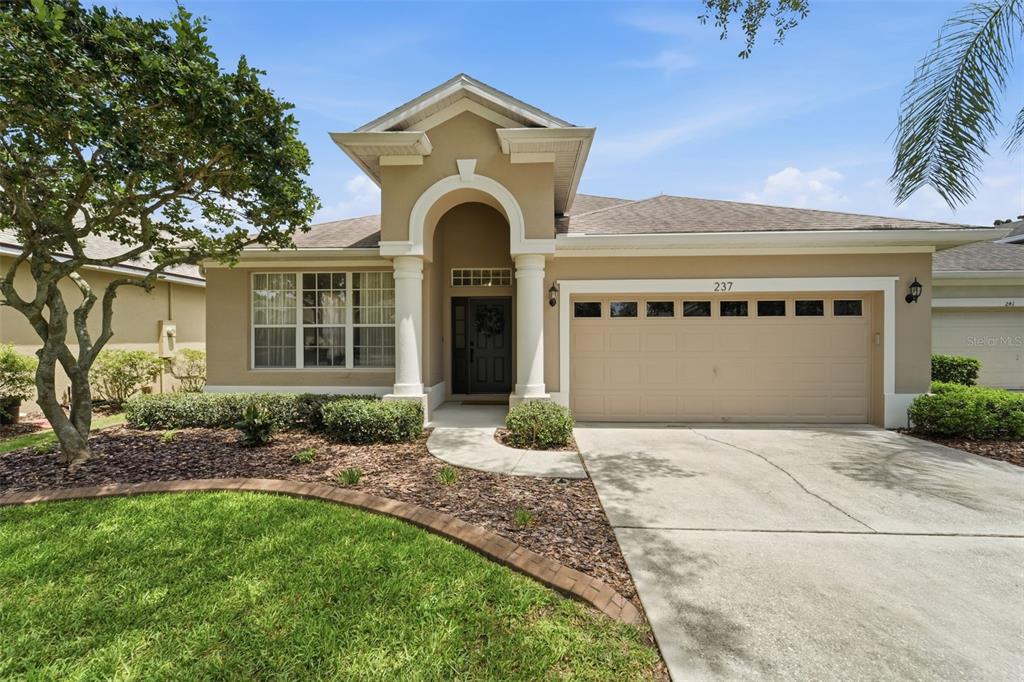 A beige single-story house features a prominent arched entryway, a two-car garage, and landscaping — 237 BRASSINGTON DRIVE, DEBARY, FL