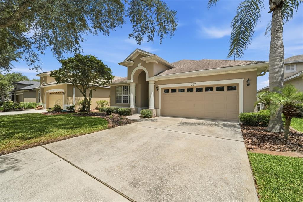A single-story tan house with a two-car garage and a paved driveway — 237 BRASSINGTON DRIVE, DEBARY, FL