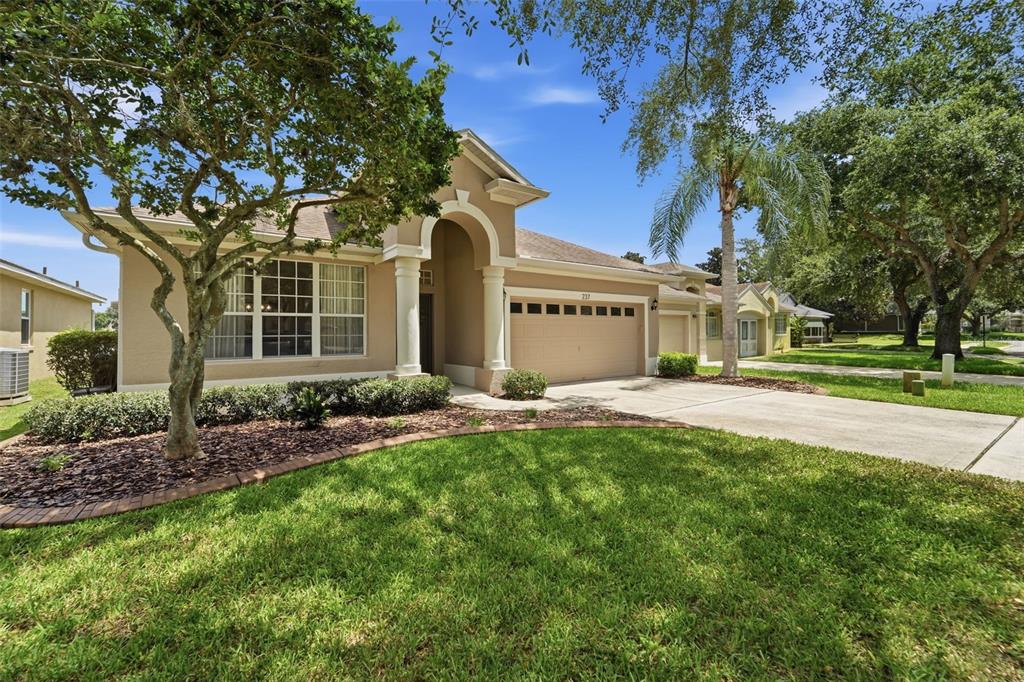 A tan single-story house with a two-car garage, arched entryway, and a manicured front lawn — 237 BRASSINGTON DRIVE, DEBARY, FL