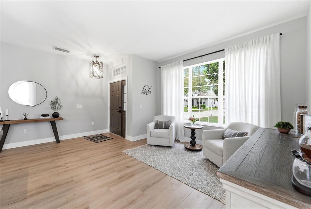 A bright living room features light wood flooring, two armchairs, and a large front window — 237 BRASSINGTON DRIVE, DEBARY, FL
