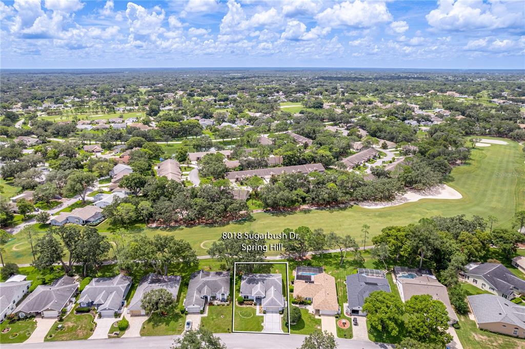 An aerial view shows a residential street with a highlighted house bordering a golf course — 8018 SUGARBUSH DRIVE, SPRING HILL, FL