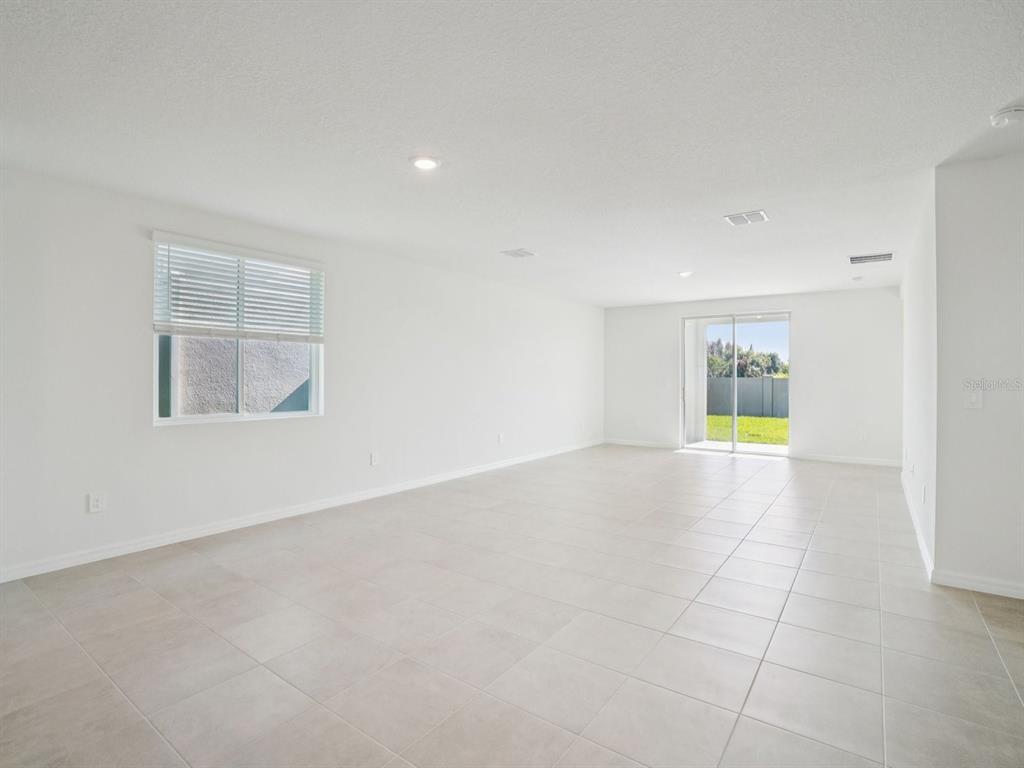 A bright, empty living room with white walls, light tile flooring, and a sliding glass door — 1696 COOLRIDGE PLACE, ZEPHYRHILLS, FL