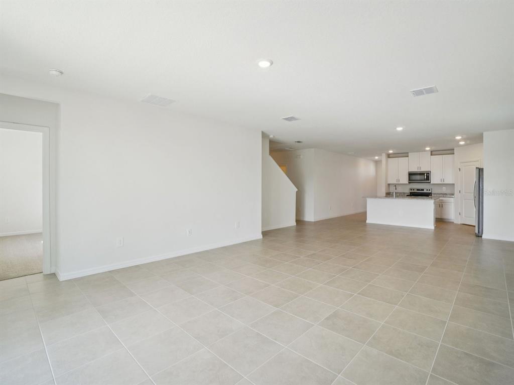 An open-concept living area with tile flooring leads to a kitchen with white cabinets — 1696 COOLRIDGE PLACE, ZEPHYRHILLS, FL