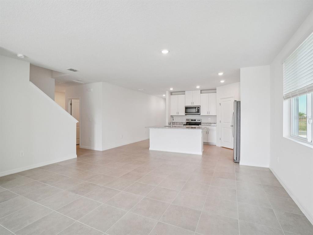 An open-concept kitchen and living area featuring white cabinets, tile flooring, and a center island — 1696 COOLRIDGE PLACE, ZEPHYRHILLS, FL