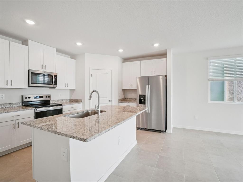 A modern kitchen features white cabinets, granite countertops, stainless steel appliances, and a central island — 1696 COOLRIDGE PLACE, ZEPHYRHILLS, FL