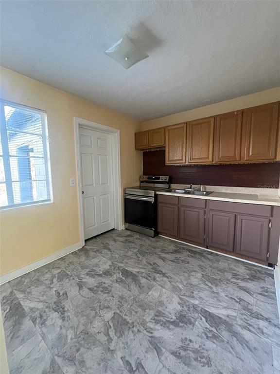 A kitchen features light-colored walls, wood cabinets, a stainless steel stove, and gray flooring — 5353 N ORANGE BLOSSOM TRAIL, MOUNT DORA, FL