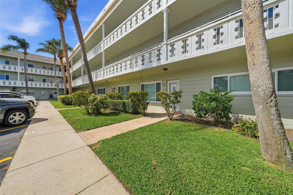 A three-story apartment building with a white balcony railing and a landscaped front lawn — 2401 ECUADORIAN WAY UNIT 19, CLEARWATER, FL