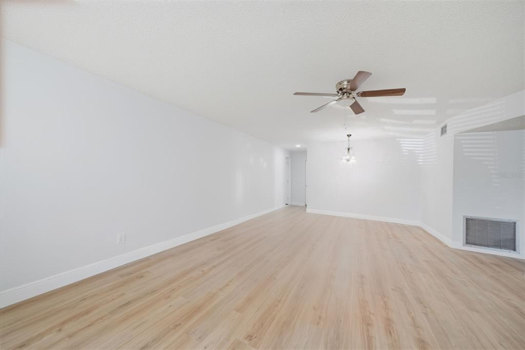 An empty living room with light wood-look flooring, white walls, and a ceiling fan — 2401 ECUADORIAN WAY UNIT 19, CLEARWATER, FL