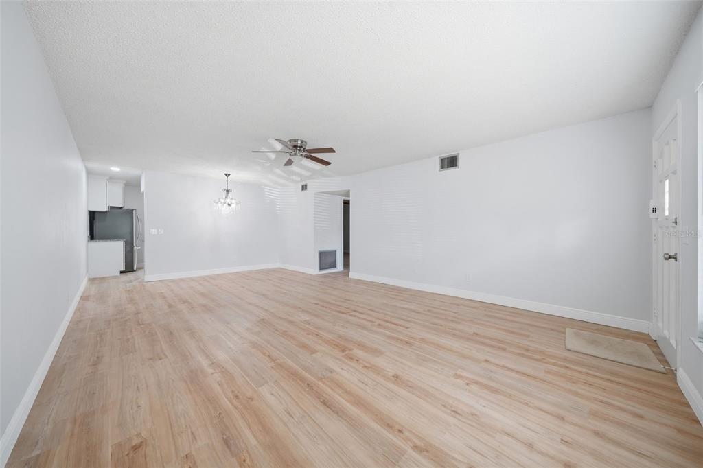 An empty living room with light wood-look flooring, white walls, and a ceiling fan — 2401 ECUADORIAN WAY UNIT 19, CLEARWATER, FL