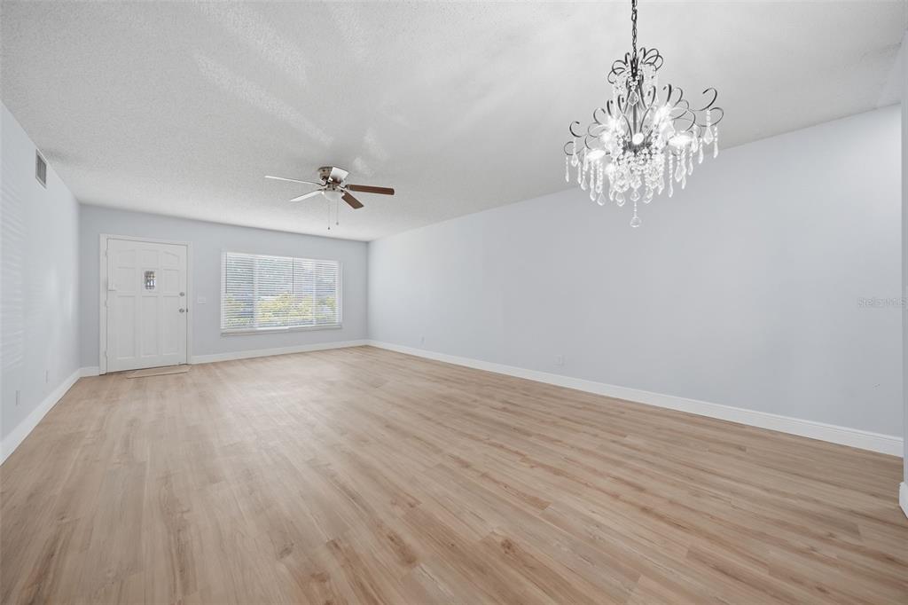 An empty living room features light wood-look flooring, white walls, a ceiling fan, and a chandelier — 2401 ECUADORIAN WAY UNIT 19, CLEARWATER, FL