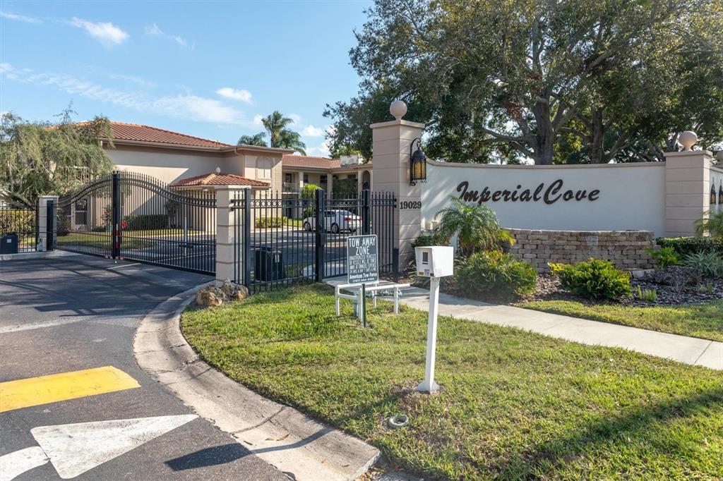 The gated entrance to the Imperial Cove community features a stone wall and landscaping — 19029 US HIGHWAY 19 N UNIT 7-8, CLEARWATER, FL