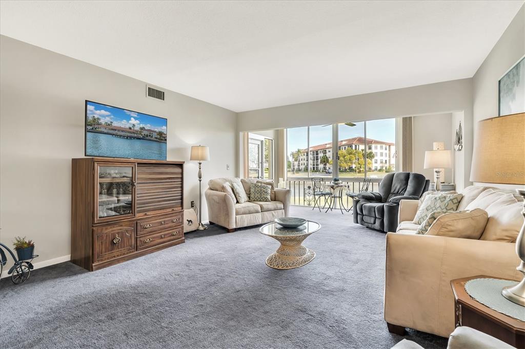 A living room with gray carpet, a wooden media console, and a view of a building — 19029 US HIGHWAY 19 N UNIT 7-8, CLEARWATER, FL
