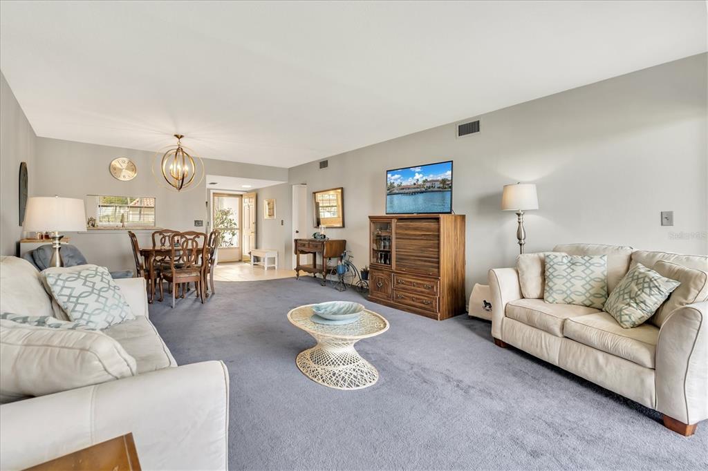 A living room with gray carpeting, two beige sofas, a dining area, and a television — 19029 US HIGHWAY 19 N UNIT 7-8, CLEARWATER, FL