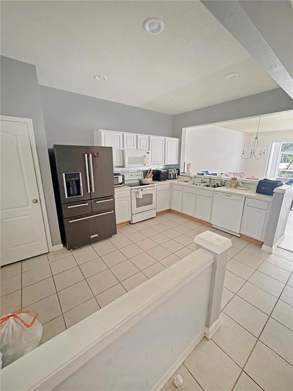 A kitchen features white cabinetry, a dark refrigerator, tile flooring, and a pass-through window — 4924 CHATHAM GATE DRIVE, RIVERVIEW, FL