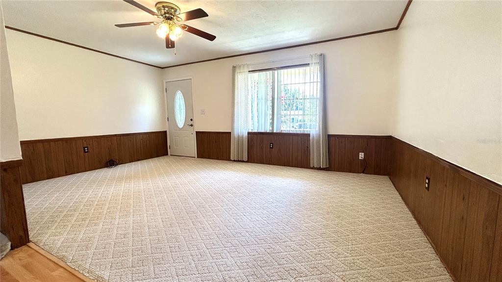 A living room features beige carpet, wood wainscoting, a ceiling fan, and a front door — 234 SW HAVANNA WAY, LAKE CITY, FL