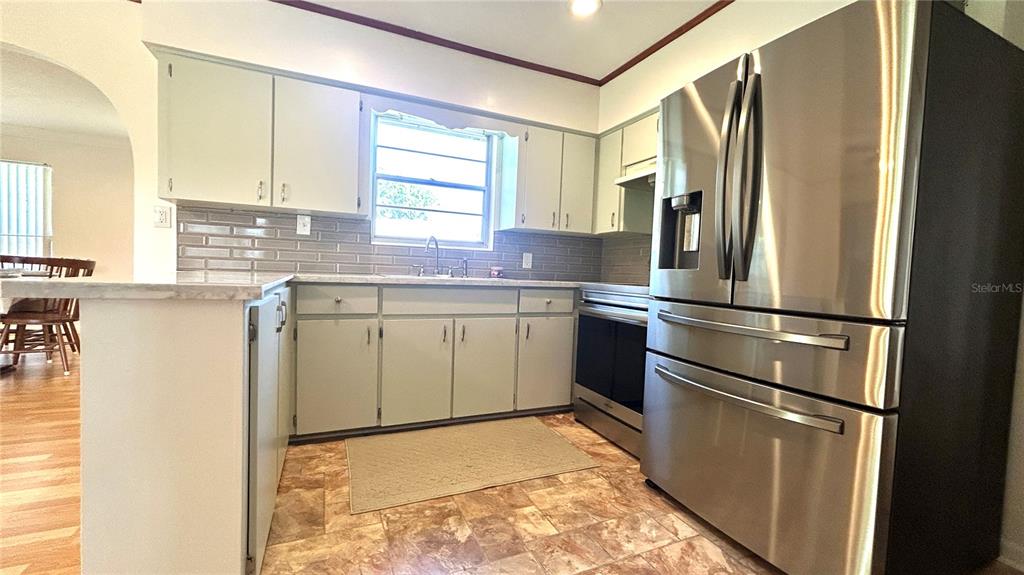 A kitchen features light-colored cabinets, stainless steel appliances, a gray tile backsplash, and tile flooring — 234 SW HAVANNA WAY, LAKE CITY, FL