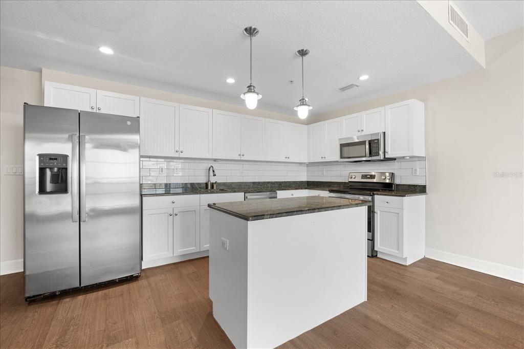 A kitchen features white cabinets, stainless steel appliances, a granite island, and wood-look flooring — 536 BAHIA BEACH BOULEVARD UNIT 422B, RUSKIN, FL