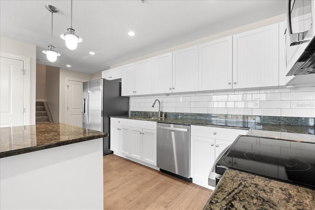 A kitchen features white cabinets, dark granite countertops, stainless steel appliances, and wood-look flooring — 536 BAHIA BEACH BOULEVARD UNIT 422B, RUSKIN, FL