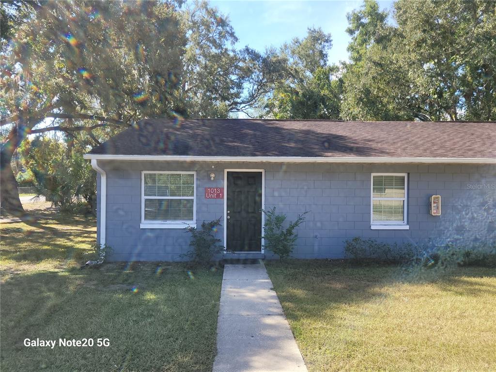 A single-story gray concrete block building with a black front door and a concrete walkway — 1013 BEECHER STREET Unit 1, LEESBURG, FL
