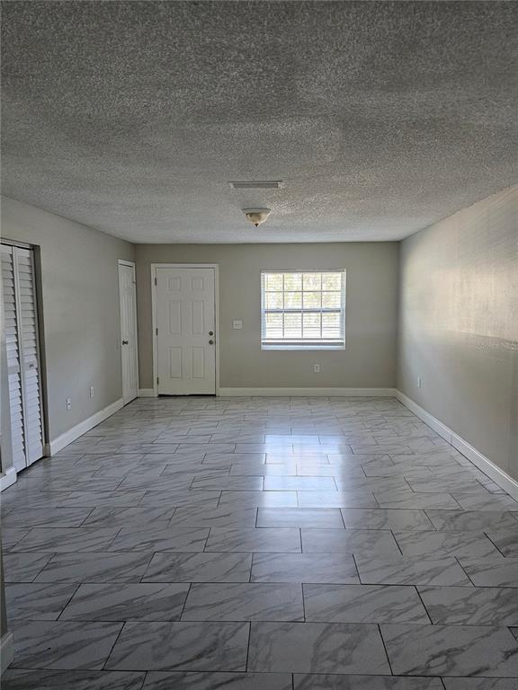 An empty room features light gray walls, white marble-look tile flooring, and a white door — 1013 BEECHER STREET Unit 1, LEESBURG, FL