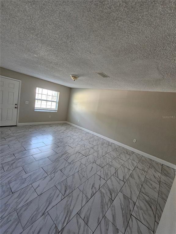 An empty room features light-colored walls, a textured ceiling, and white marble-patterned tile flooring — 1013 BEECHER STREET Unit 1, LEESBURG, FL