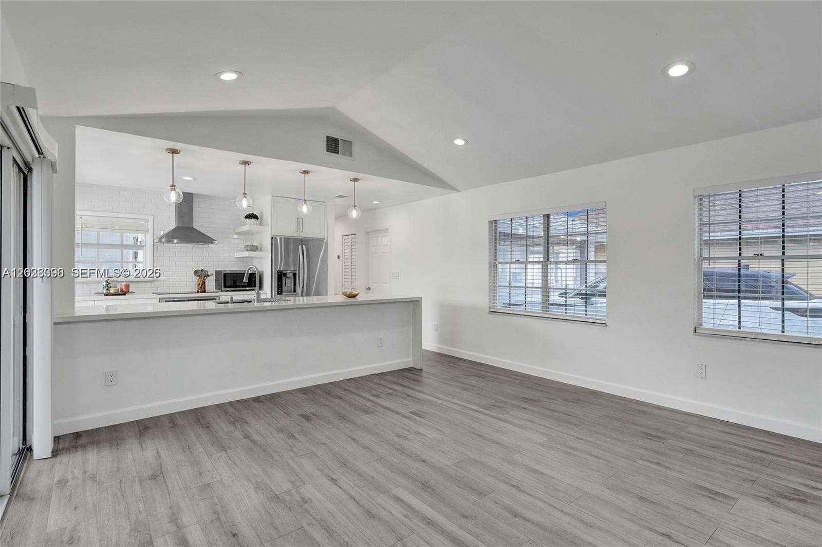 A bright, open-concept kitchen and living area features white walls, gray wood-look flooring, and vaulted ceilings — 14049 SW 103rd Ter # 1, Miami FL 33186, MIAMI, FL