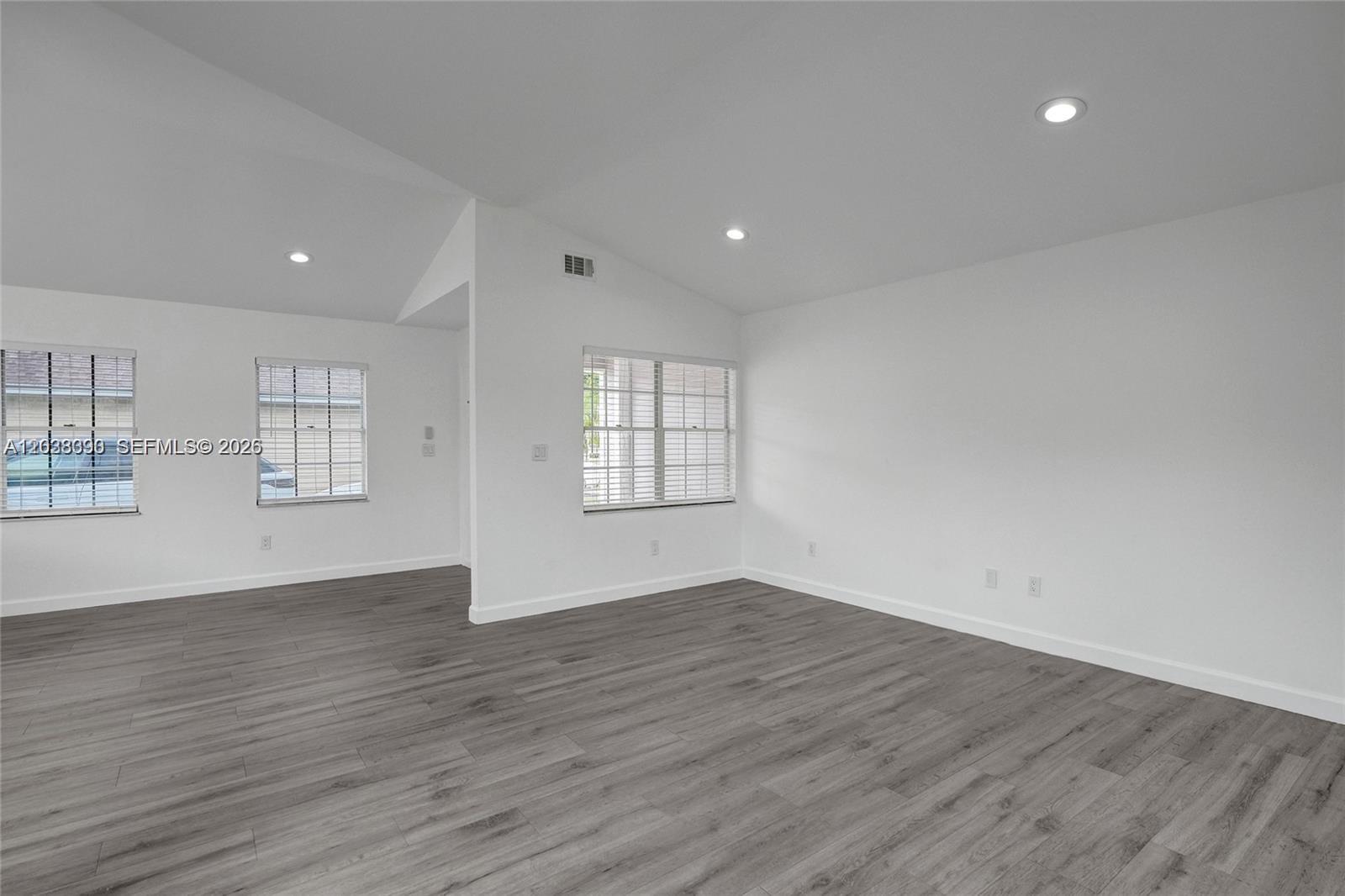 An empty room features white walls, vaulted ceilings with recessed lighting, and gray wood-look flooring — 14049 SW 103rd Ter # 1, Miami FL 33186, MIAMI, FL