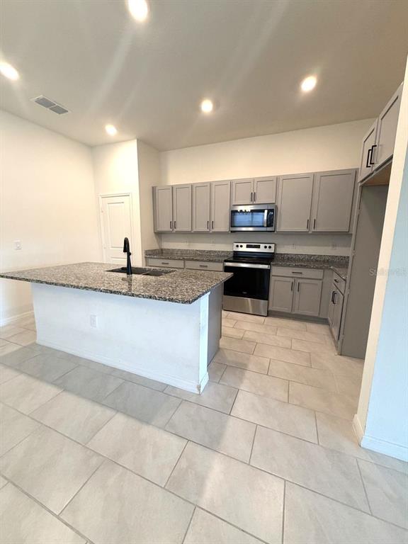 A kitchen features gray cabinets, granite countertops, a center island, and light-colored tile flooring — 925 OVERPOOL AVENUE, DAVENPORT, FL