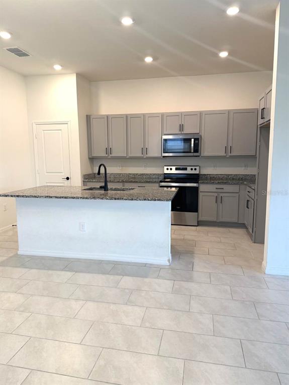 A kitchen features gray cabinets, granite countertops, a center island, and stainless steel appliances — 925 OVERPOOL AVENUE, DAVENPORT, FL