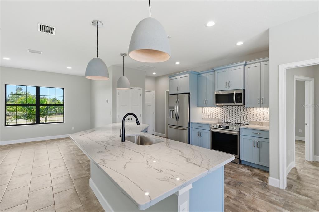 A kitchen features a marble-topped island, light blue cabinets, stainless steel appliances, and pendant lighting — 14364 APPLETON BOULEVARD, PORT CHARLOTTE, FL