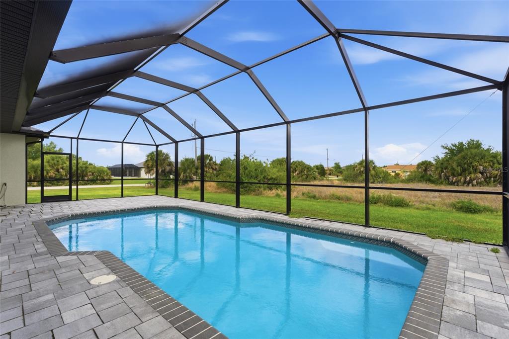 A swimming pool with a paved deck is enclosed by a screened lanai overlooking grass — 14364 APPLETON BOULEVARD, PORT CHARLOTTE, FL