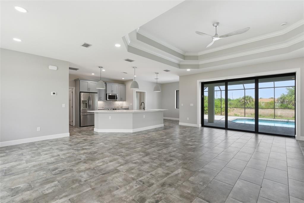 An open-concept kitchen and living area features gray tile flooring, a tray ceiling, and pool views — 14364 APPLETON BOULEVARD, PORT CHARLOTTE, FL
