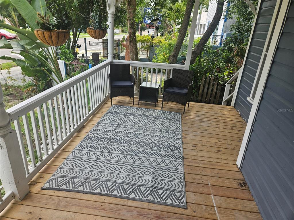 A wooden front porch features two wicker chairs, a small table, and a patterned rug — 318 E TARPON AVENUE UNIT A1, TARPON SPRINGS, FL