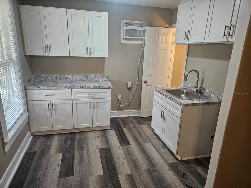 A kitchen features white cabinets, granite-look countertops, a stainless steel sink, and wood-look flooring — 318 E TARPON AVENUE UNIT A1, TARPON SPRINGS, FL
