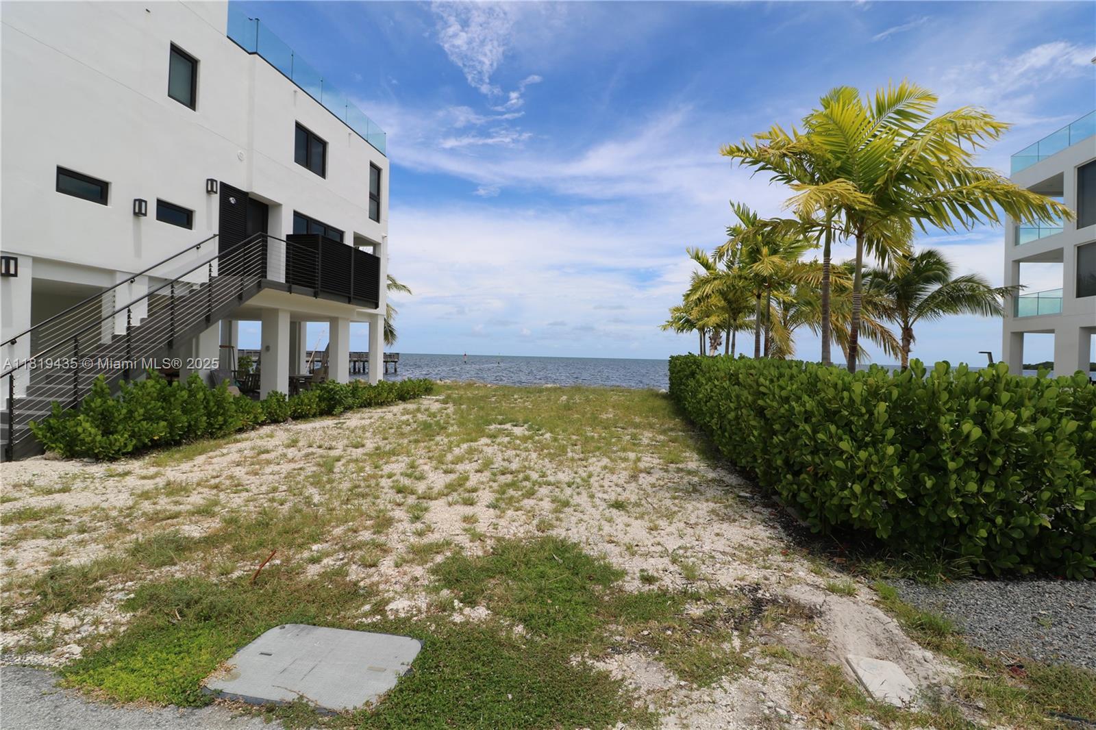 A sandy path leads between two modern white buildings toward the ocean under blue skies — 94825 Overseas Hwy #35, Key Largo FL 33037, KEY LARGO, FL