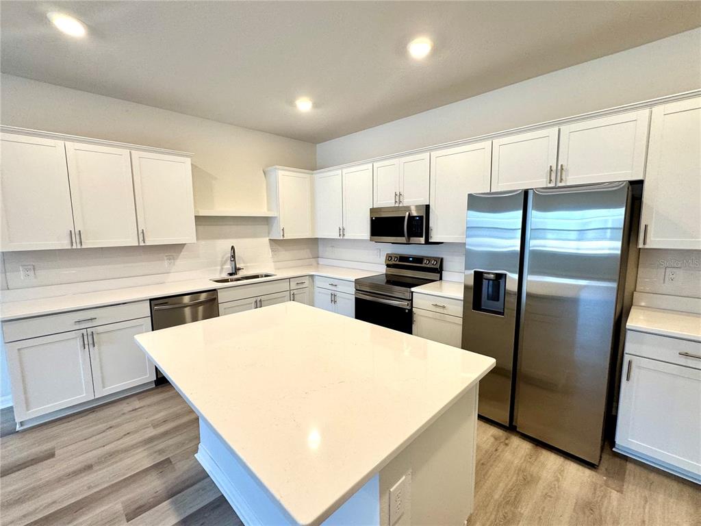 A modern kitchen features white cabinets, a large quartz island, and stainless steel appliances — 5788 FRESHWATER CANYON DRIVE, ST CLOUD, FL