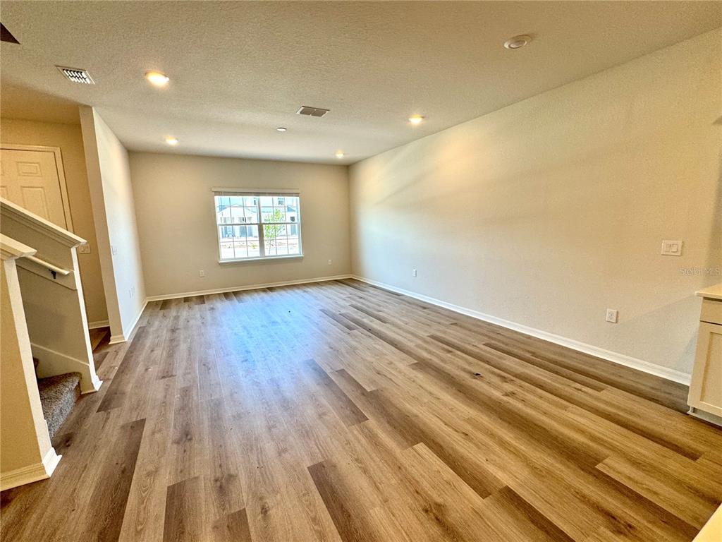 An empty living room features light-colored walls, recessed lighting, and wood-look plank flooring — 5788 FRESHWATER CANYON DRIVE, ST CLOUD, FL