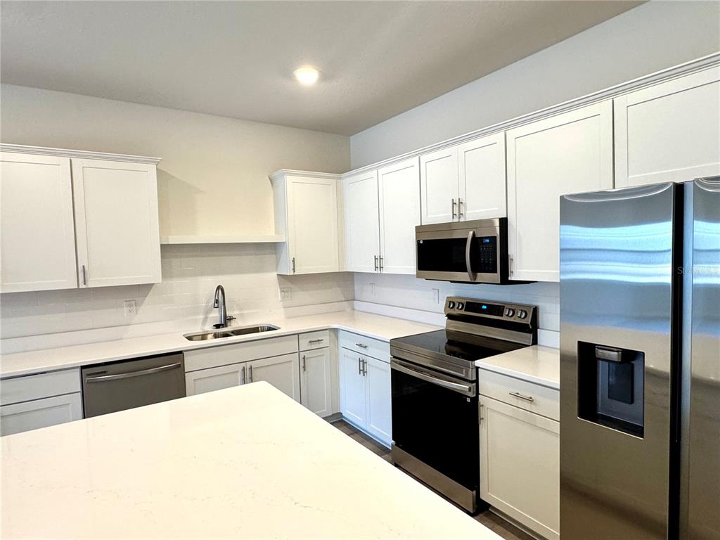 A modern kitchen features white cabinetry, stainless steel appliances, and a large white island — 5788 FRESHWATER CANYON DRIVE, ST CLOUD, FL