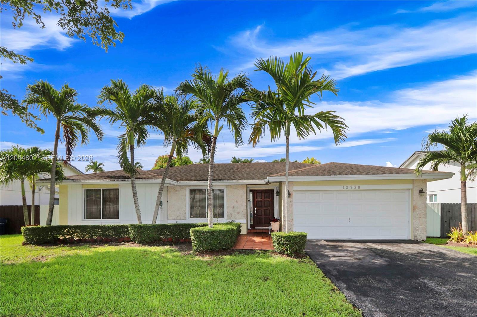A single-story house features a white facade, stone accents, a two-car garage, and palm trees — 12730 SW 119th St, Miami FL 33186, MIAMI, FL