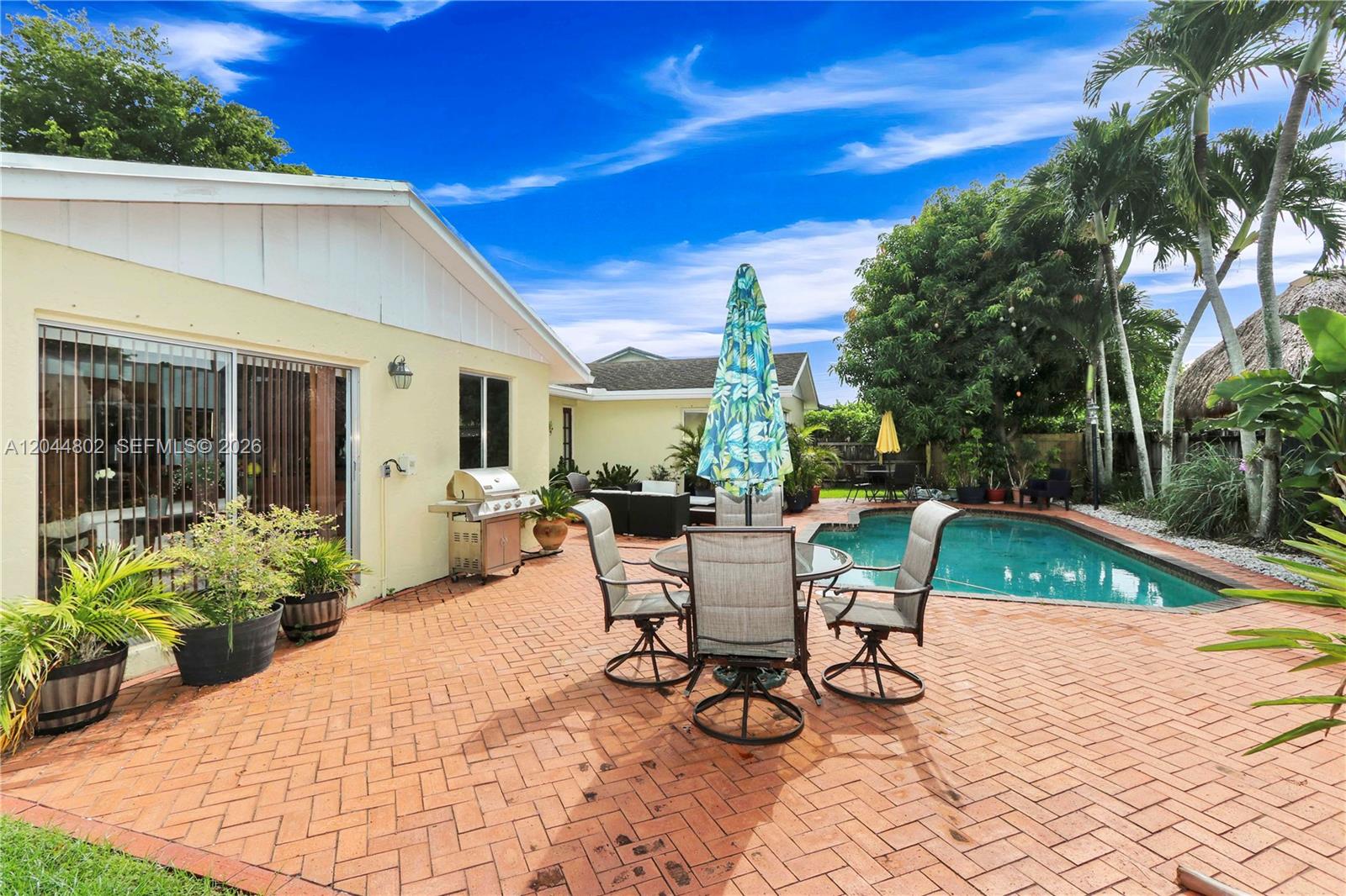 A patio with a dining set, grill, and swimming pool behind a yellow house — 12730 SW 119th St, Miami FL 33186, MIAMI, FL