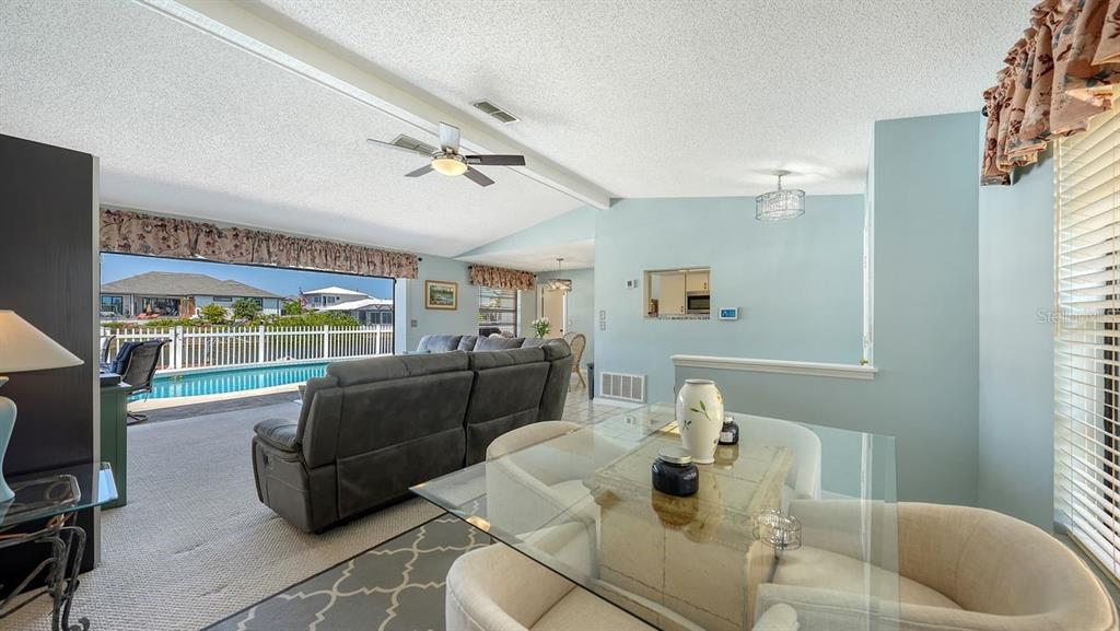 A living and dining area features a glass table, gray sofa, and a pool view — 723 PORTIA STREET N, NOKOMIS, FL